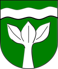 Ein Wappenschild in Grün. Darauf unter einem erhöhten silbernen (weißen) Wellenbalken ein silberner (weißer) junger, wachsender, dreiblättriger Baum.